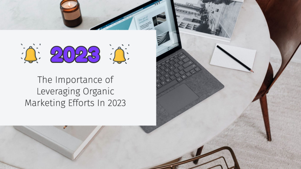 A laptop on a table next to a notepad and a pen. There is text overlay on the graphic stating "The importance of Leveraging Organic Marketing Efforts in 2023."